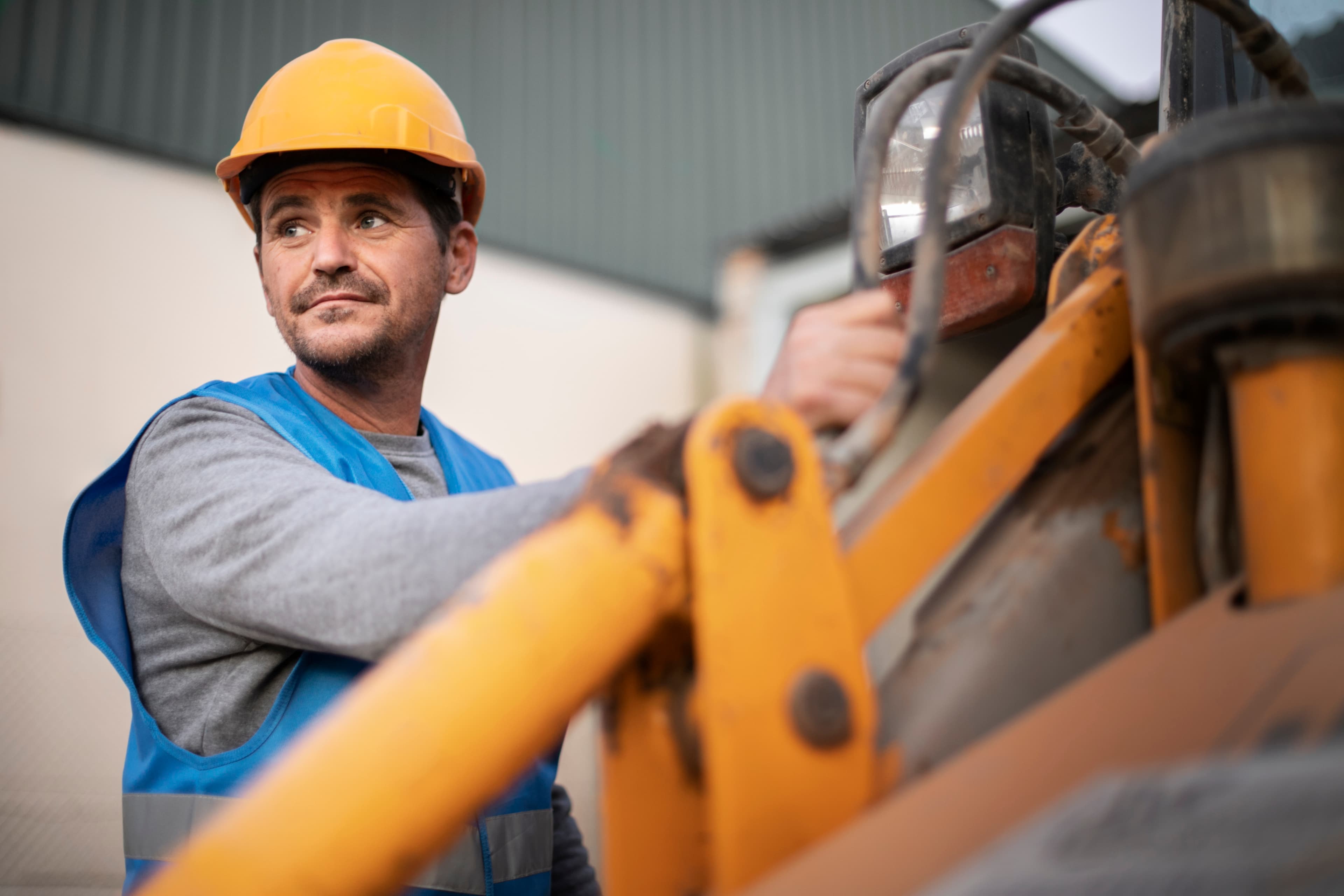 A construction worker in a hard hat and high-visibility vest climbing onto a yellow machine.